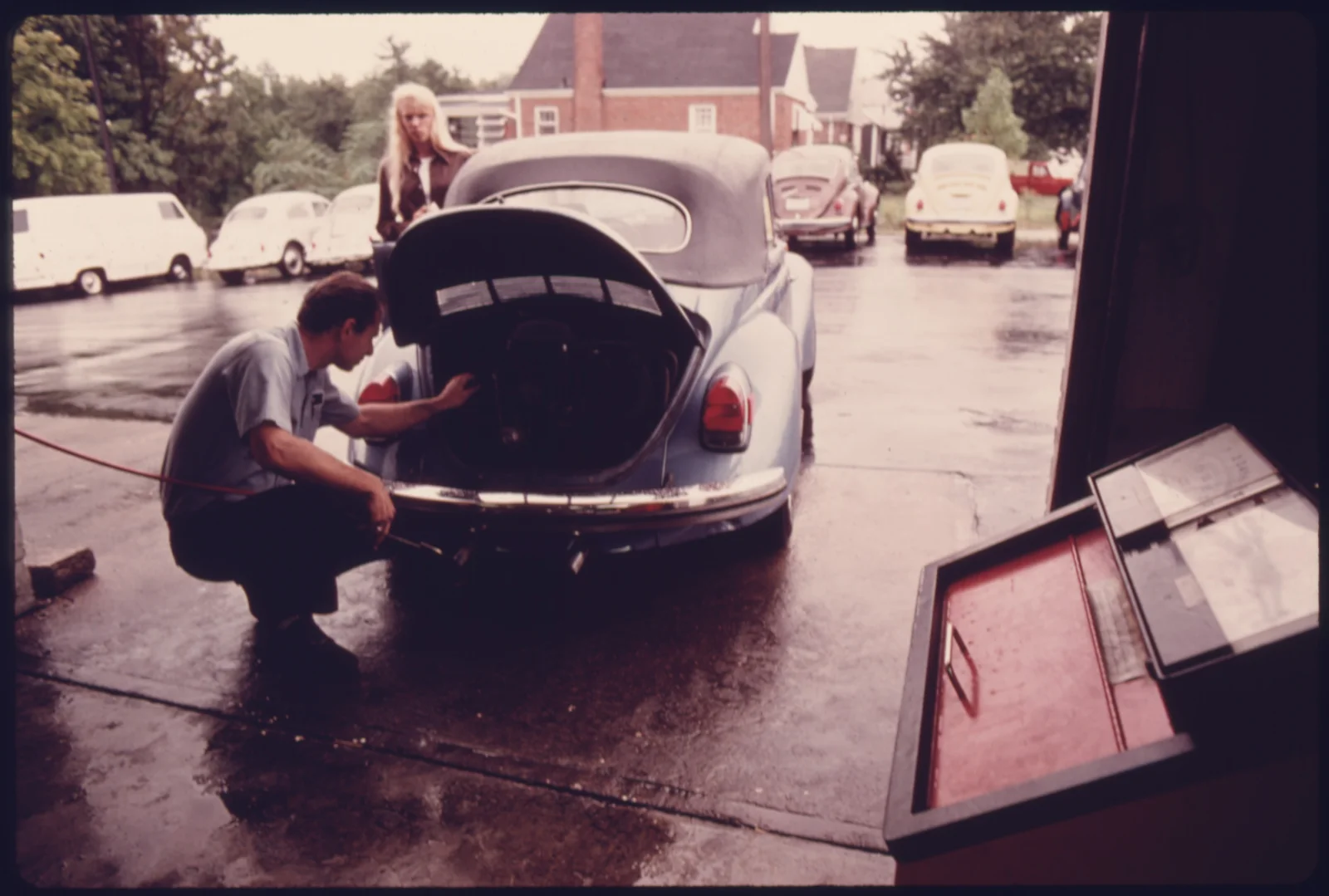 A service station mechanic adjusts the engine while a young woman watches, the classic information gap between expert and customer.
